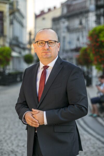 Mężczyzna w garniturze, w tle budynki